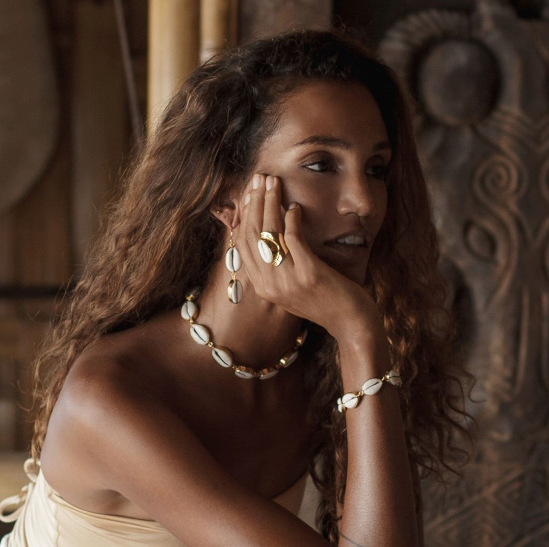 Woman wearing gold and cowrie shell jewelry with a decorative background