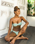 Woman wearing a aquamarine crochet bikini with a floral pattern sitting on a wooden floor.