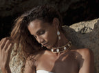Woman with gold shell necklace and earrings against a rocky background
