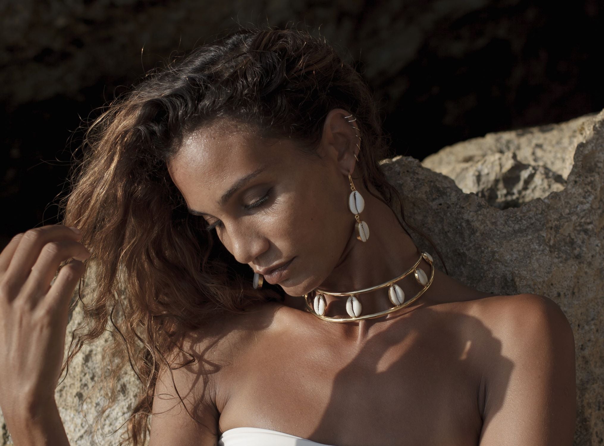 Woman with gold shell necklace and earrings against a rocky background