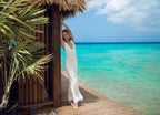 Woman in a white dress with shells standing on a wooden deck by the ocean