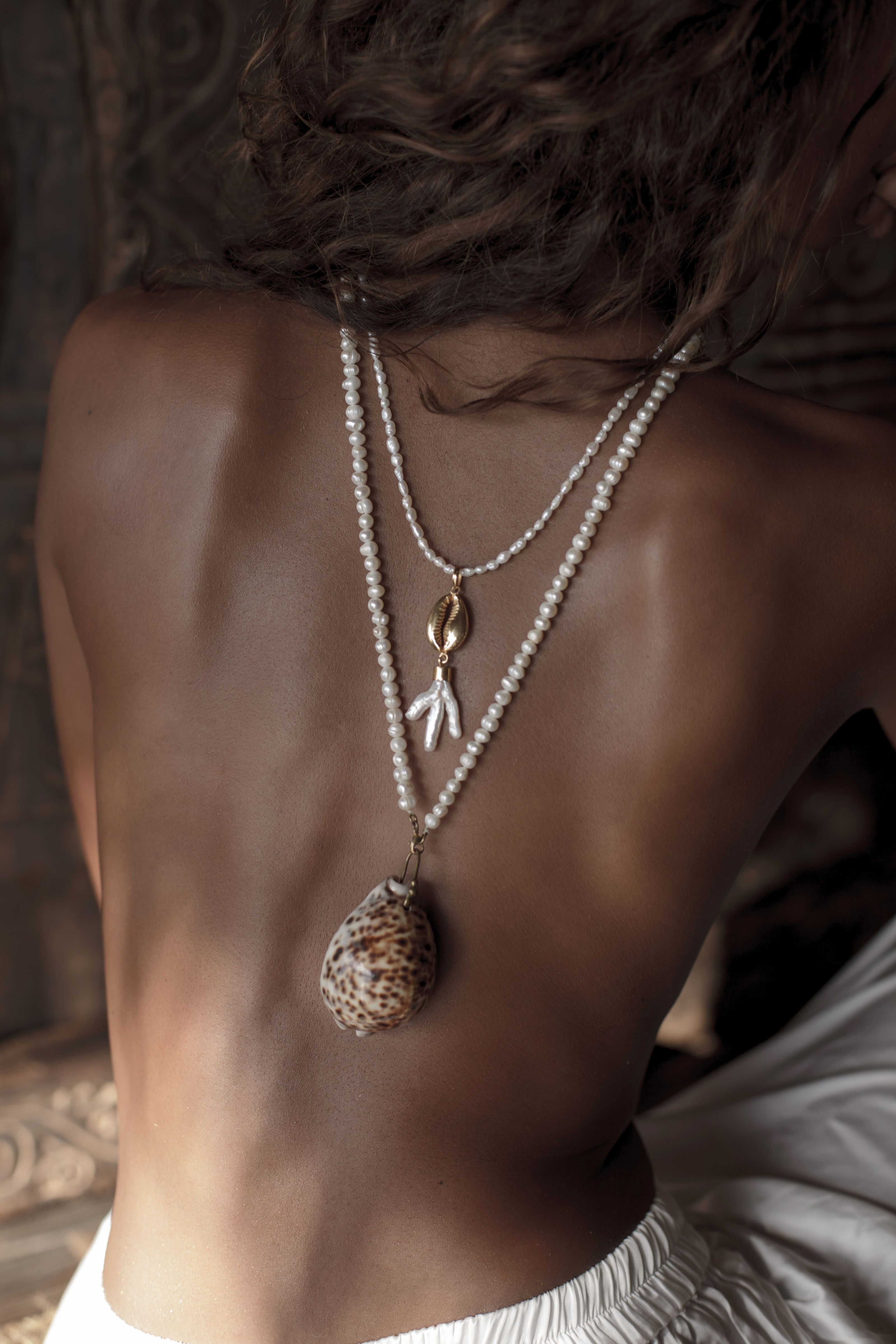 Person wearing a necklace with a shell and mother of pearl pendant on a neutral background