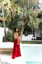 Woman in a red dress standing by a pool with tropical plants in the background